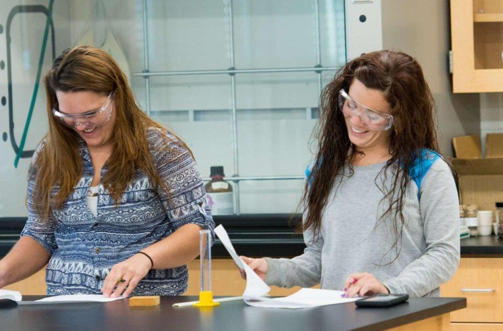 Two female students smiling as they work on a chemistry assignment together.